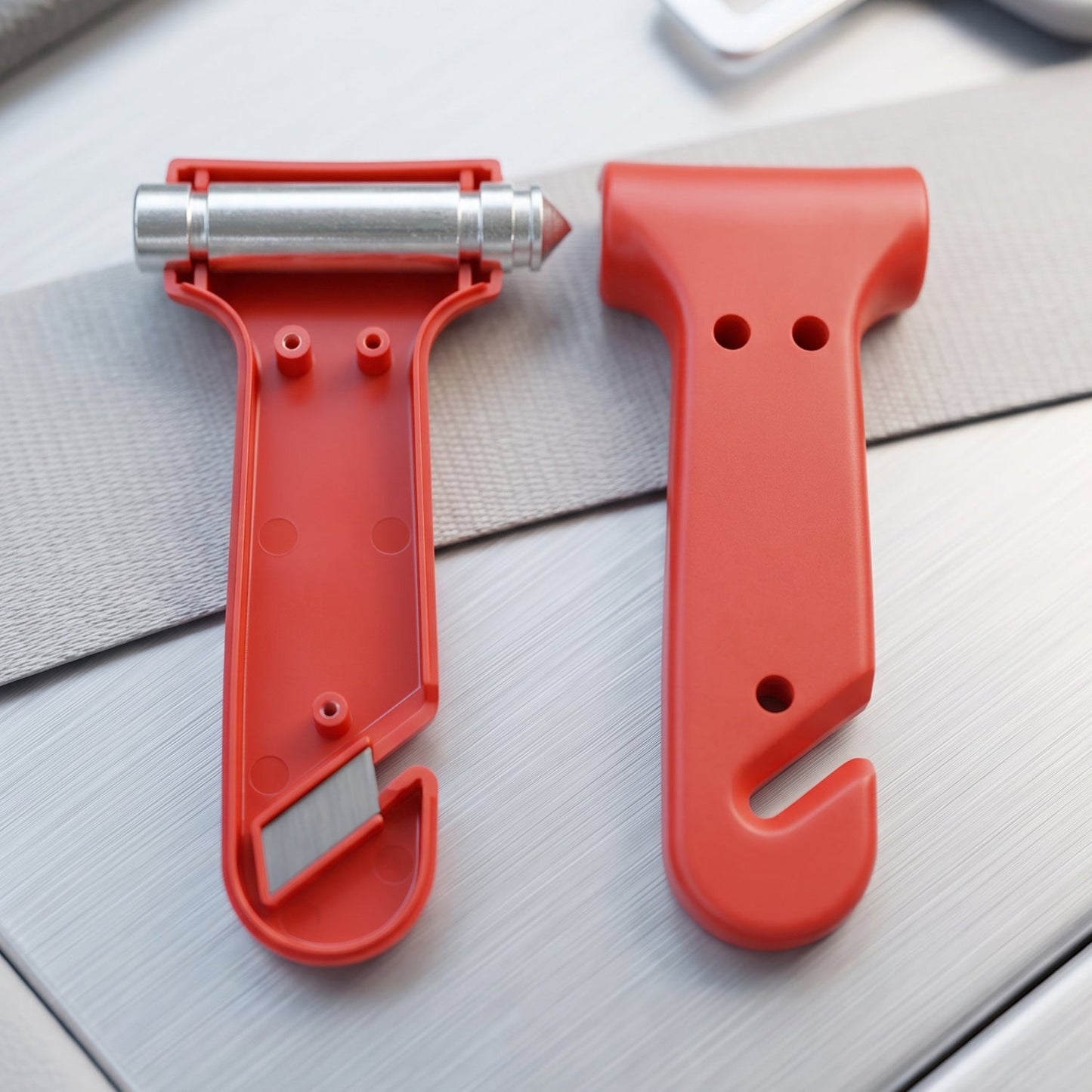 Two red car safety hammers are shown on a gray and silver surface, one disassembled to reveal the seatbelt cutter.