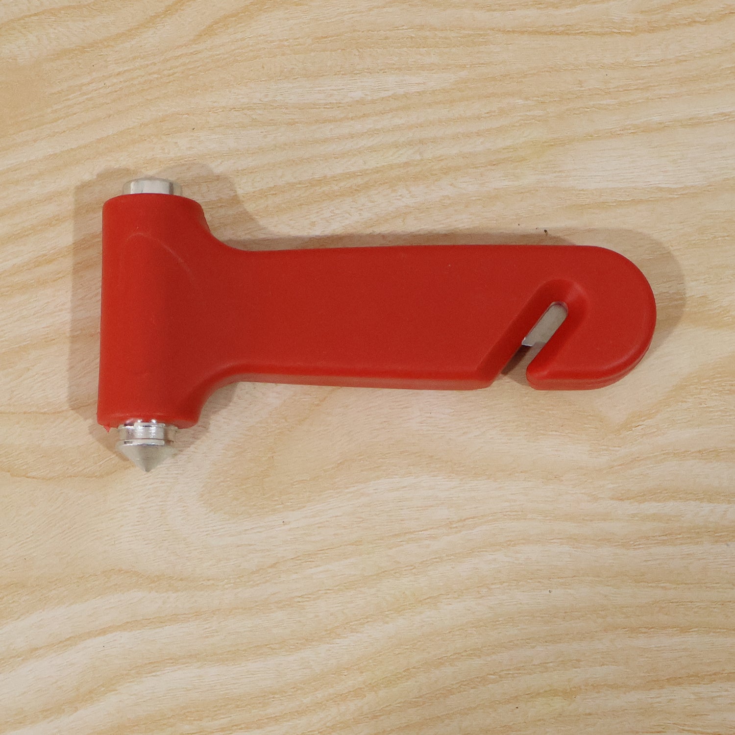 A red car safety hammer with a silver window breaker and seatbelt cutter is placed on a light wood surface.