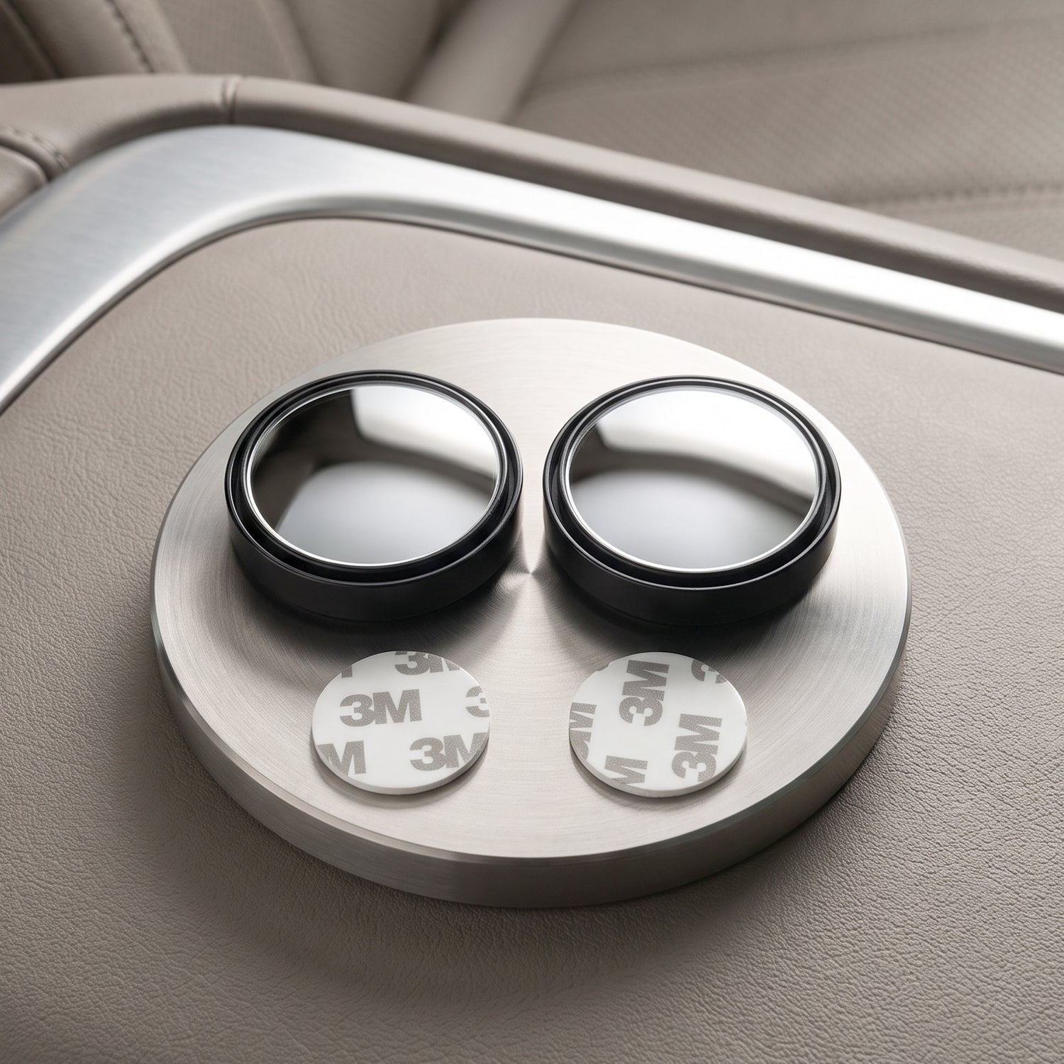 Two round blind spot mirrors with black frames and two white 3M adhesive pads on a brushed metal surface.