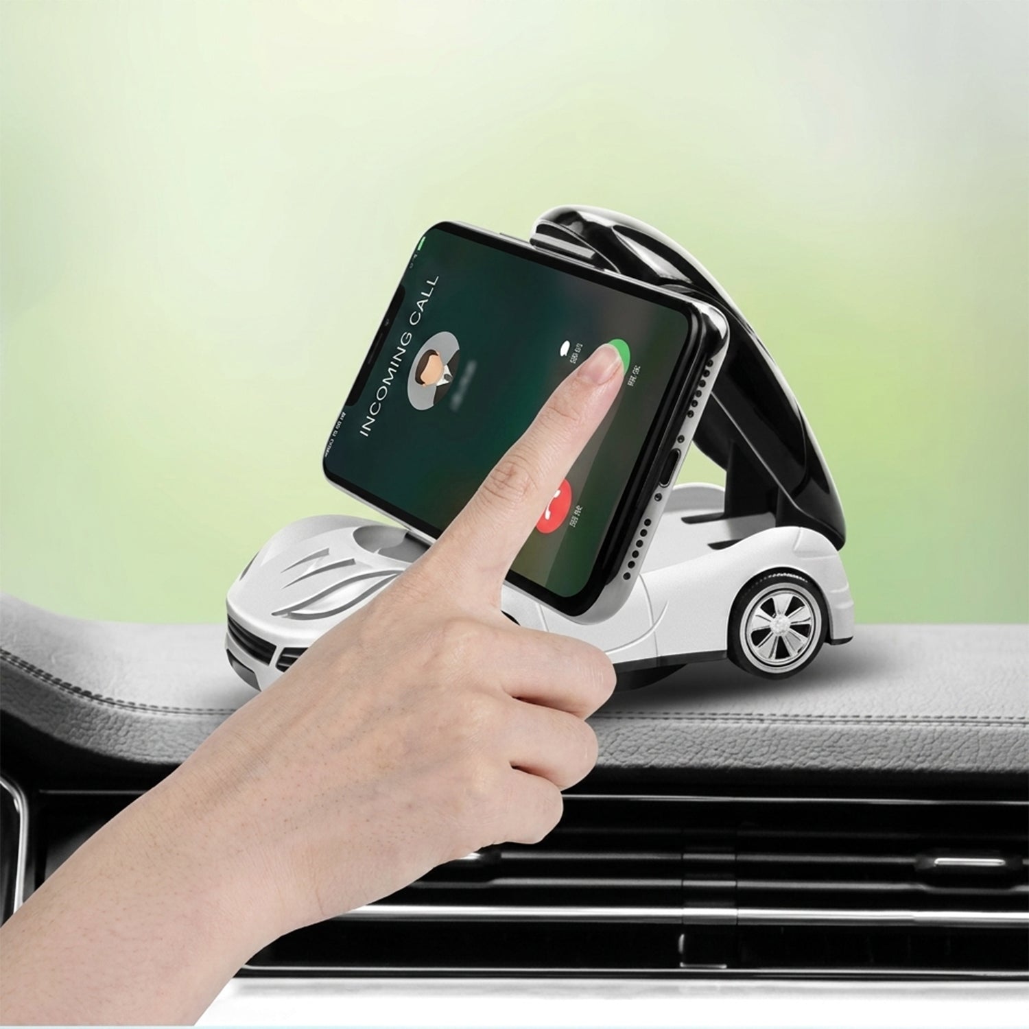 A hand touches a smartphone held upright in a white car-shaped phone holder on a car dashboard.