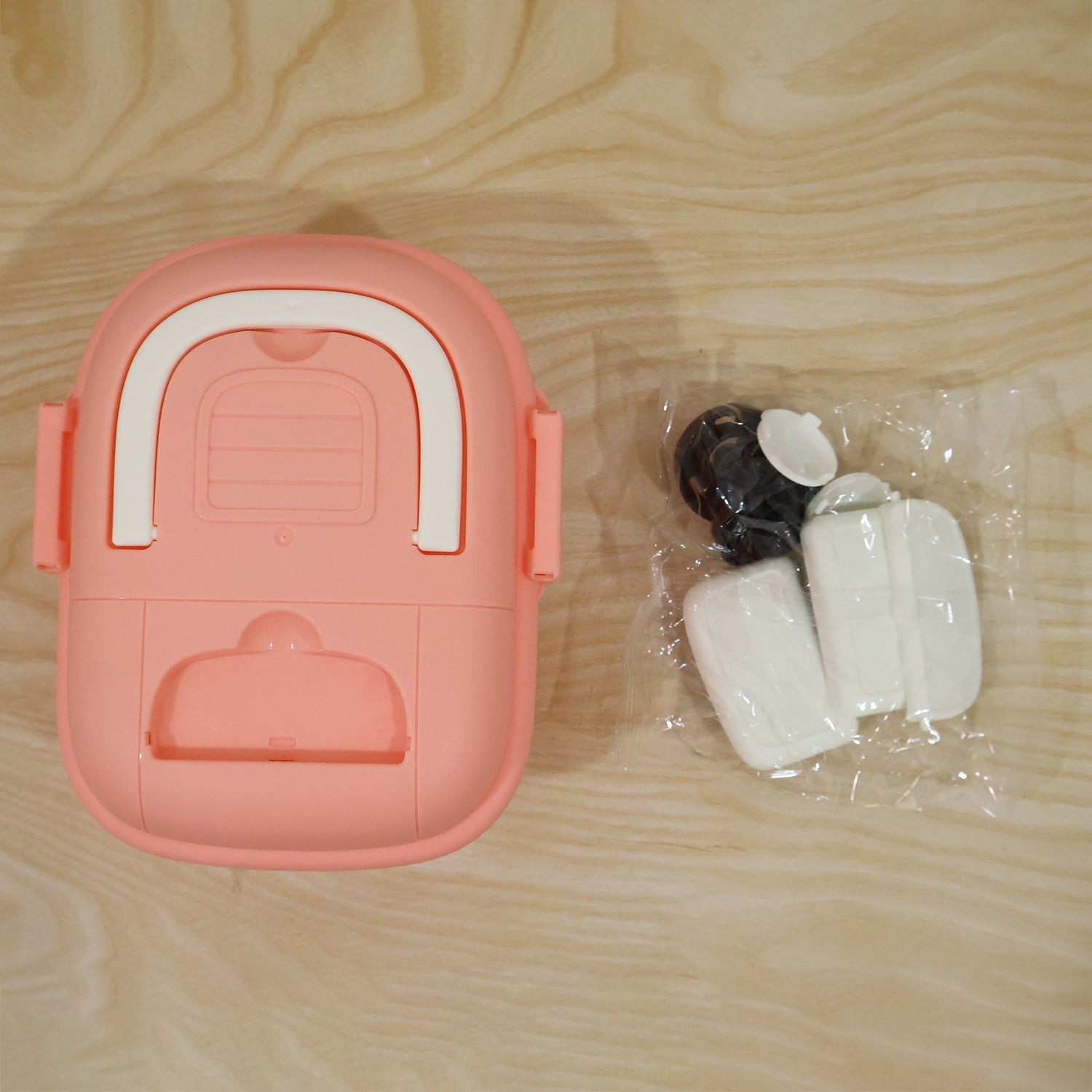 The underside of the pink fire truck toy storage box lid is shown next to a plastic bag containing white and black parts.