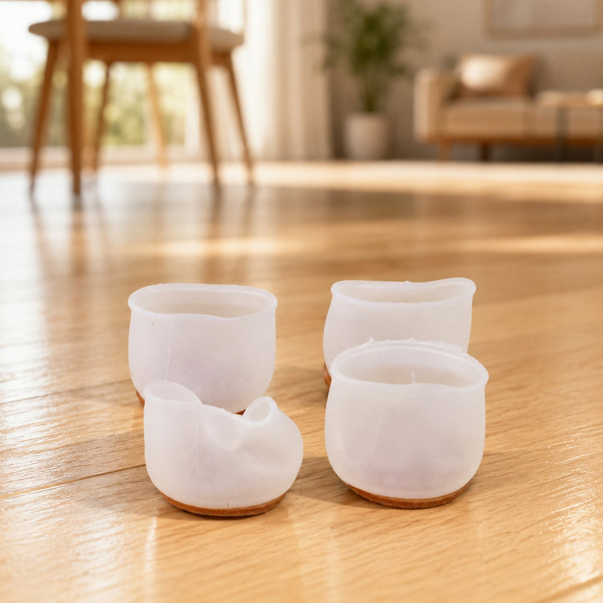 Four translucent silicone furniture leg protectors with felt bottoms on a wooden floor in a living room setting.