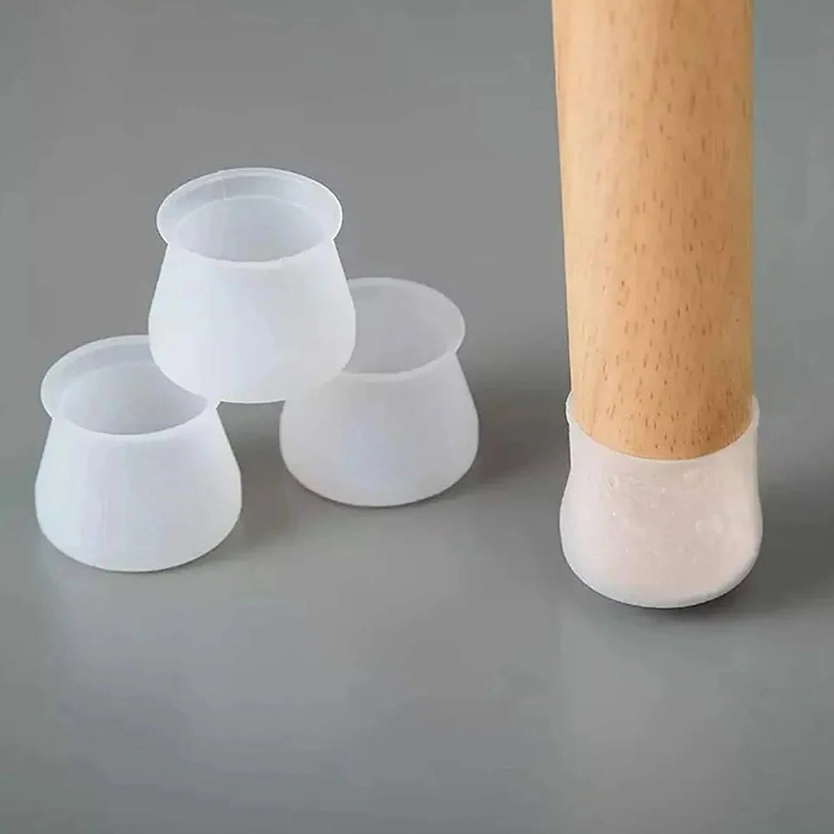 Three translucent silicone furniture leg protectors next to a wooden leg with one applied, on a gray surface.