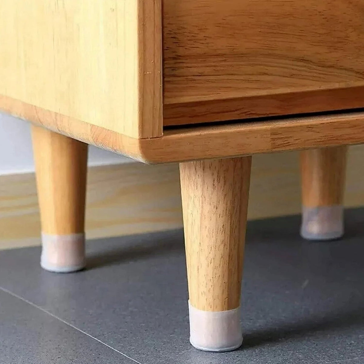 Three light wooden furniture legs with translucent silicone protectors on a gray tiled floor.