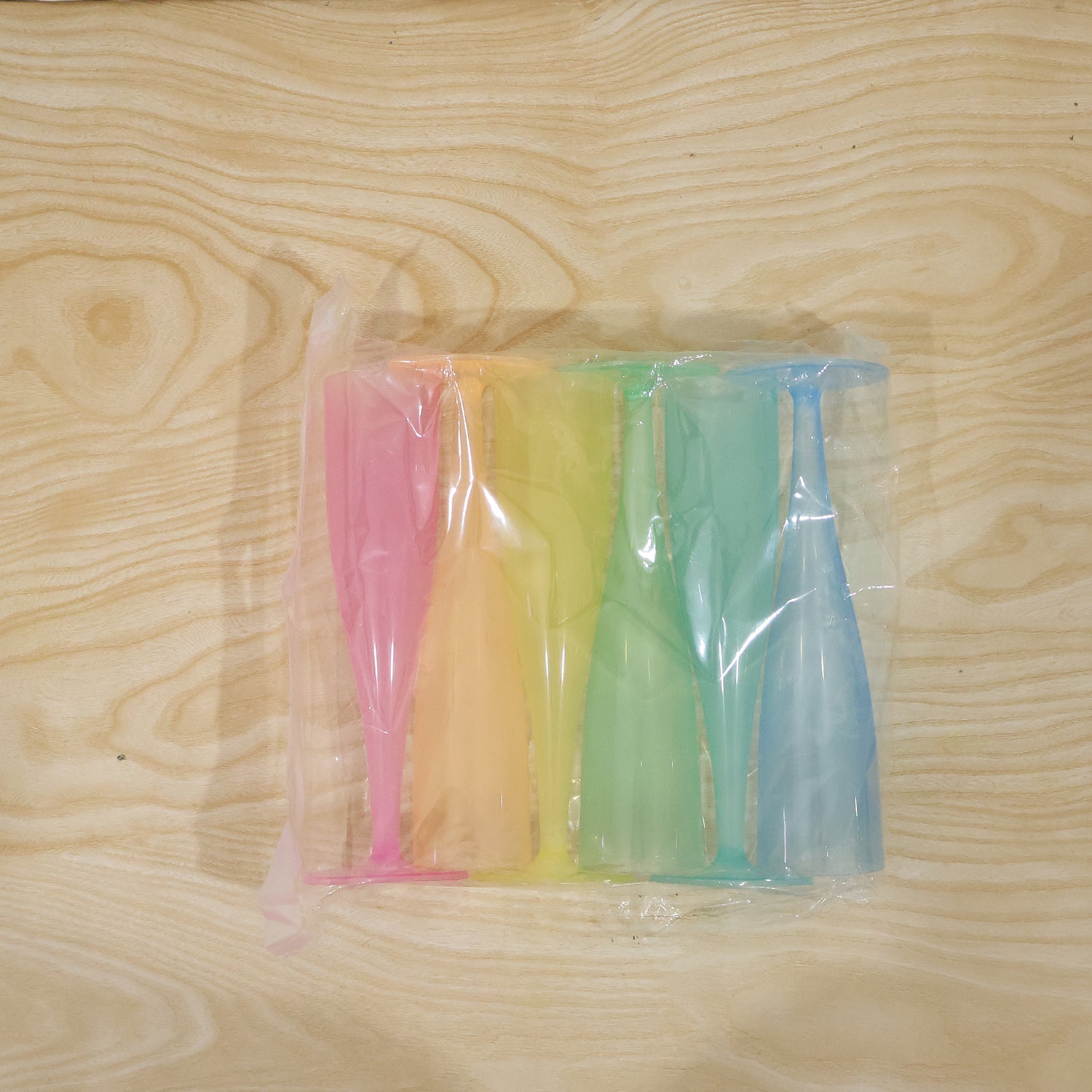Six colorful plastic champagne flutes in pink, yellow, orange, green, and blue, sealed in clear plastic packaging.