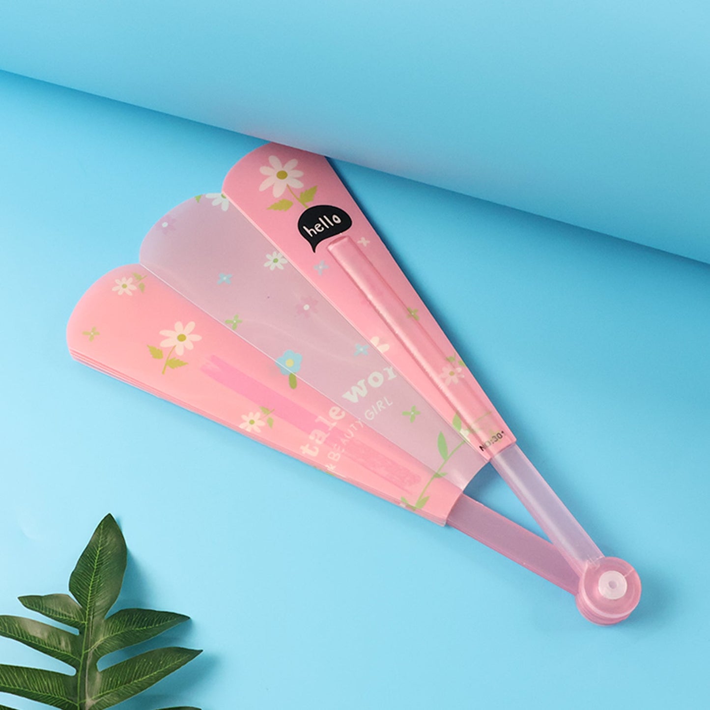 A partially open pink fan with white flowers and text, resting on a blue and white surface.