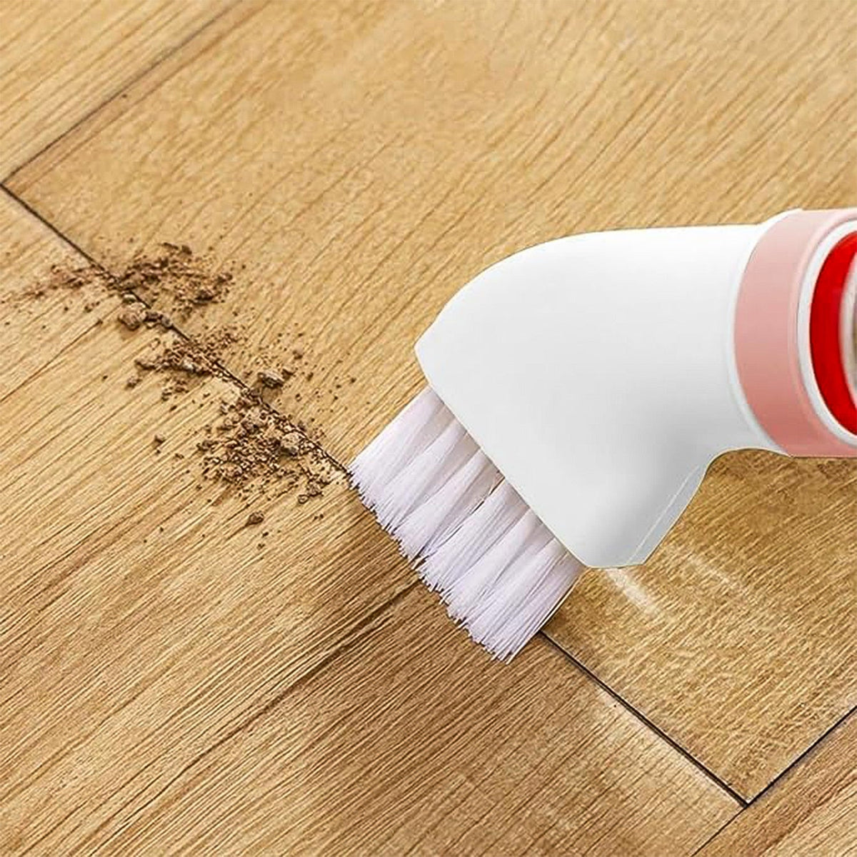 A white and pink brush attachment with white bristles cleaning a line of dirt on a wooden floor.