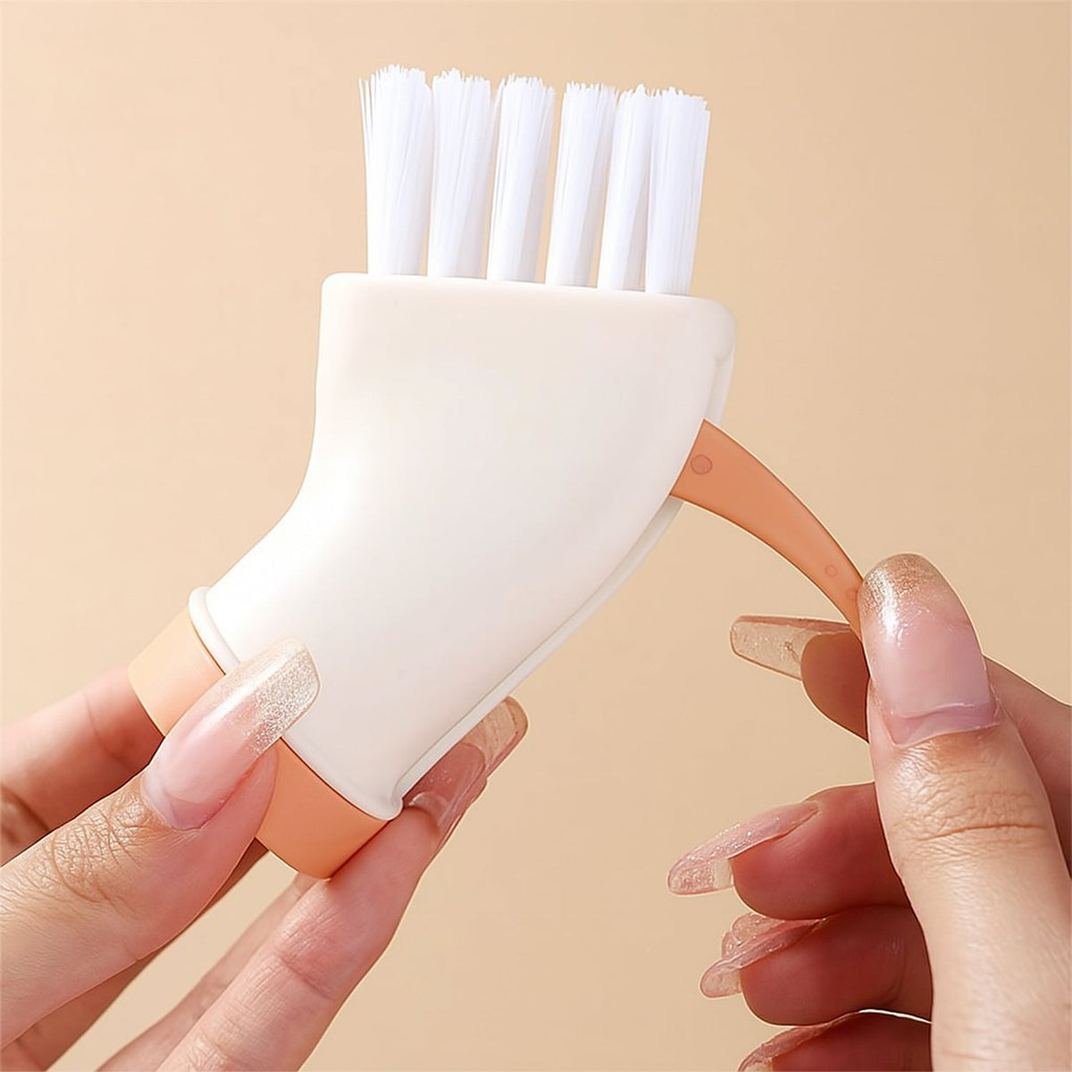 Two hands hold the cream and orange brush attachment, demonstrating the small hook remover feature.