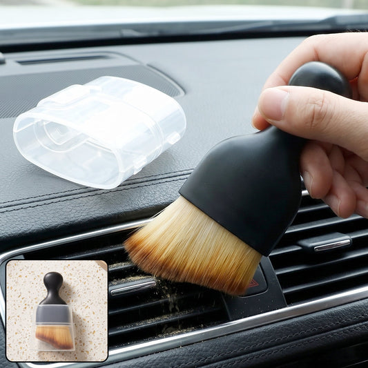 Hand holding a black brush with light brown bristles, cleaning a car's dashboard vent, with dust falling. A clear plastic
