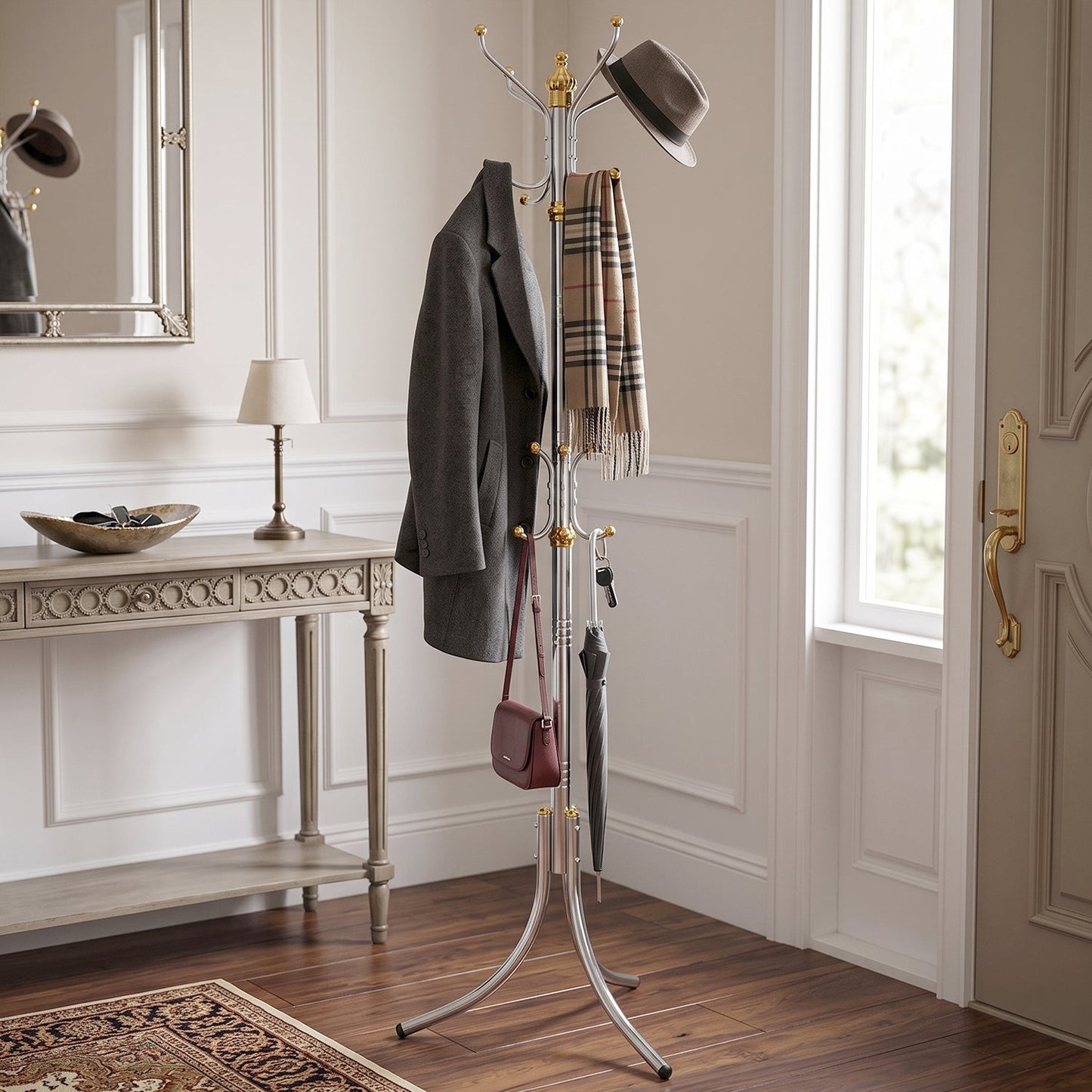 A silver and gold metal stand holds a grey coat, a plaid scarf, a brown hat, a red purse, and an umbrella in an entryway