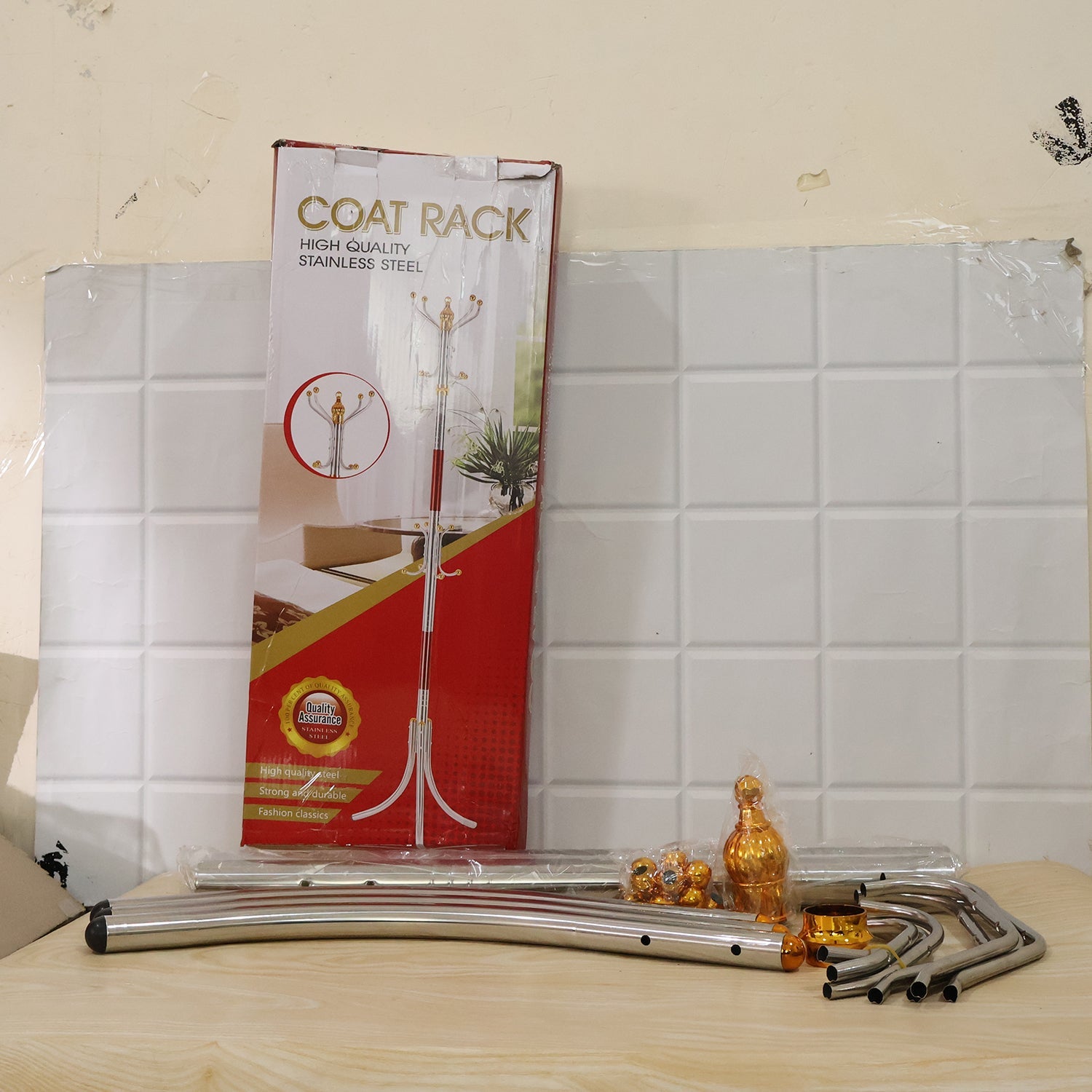 A disassembled metal clothes hanger stand with gold accents and its red and white packaging box are on a wooden surface