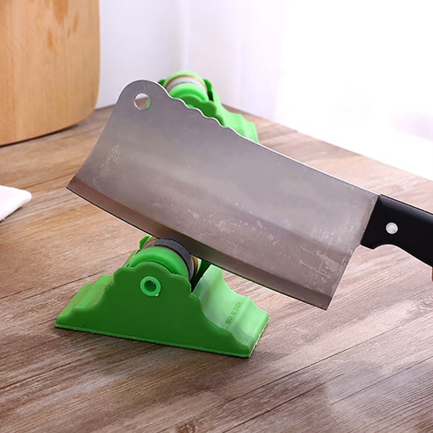 A person sharpens a cleaver on a green compact knife sharpener on a wooden surface.