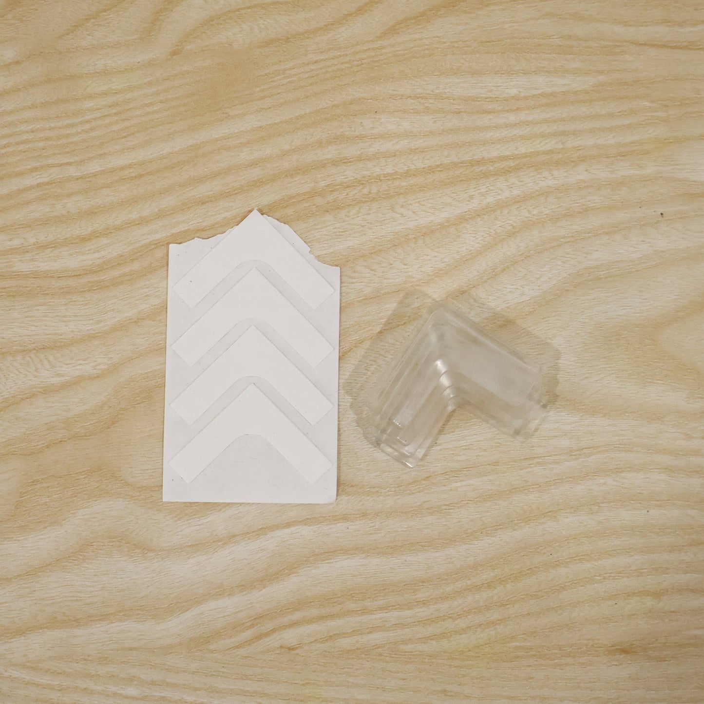 A sheet of white adhesive strips and a stack of clear silicone corner protectors rest on a light wood grain surface.