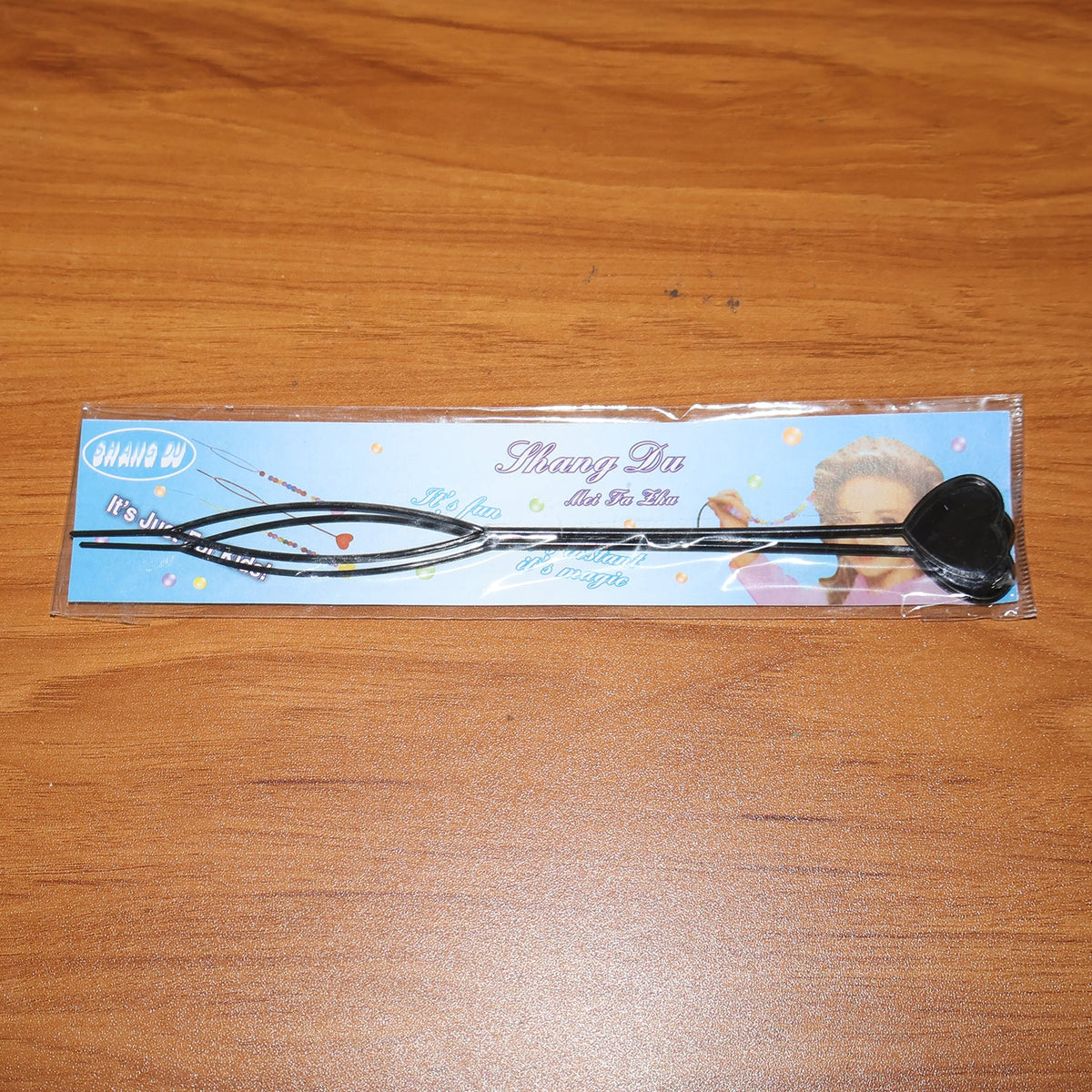 A single black heart-shaped hair styling tool sealed in clear plastic packaging on a wooden surface.
