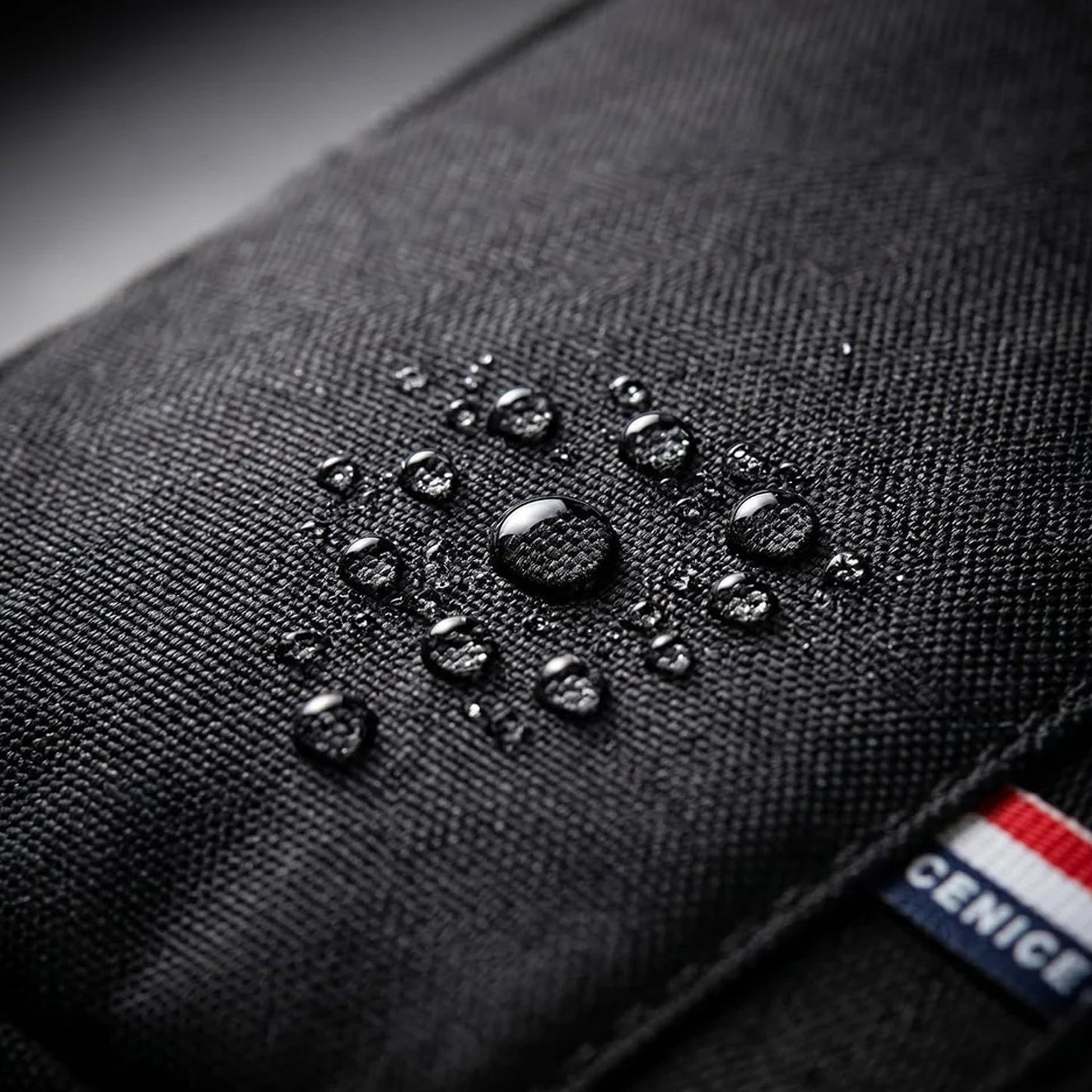 Close-up of water droplets beading on the waterproof black fabric of the sling bag.
