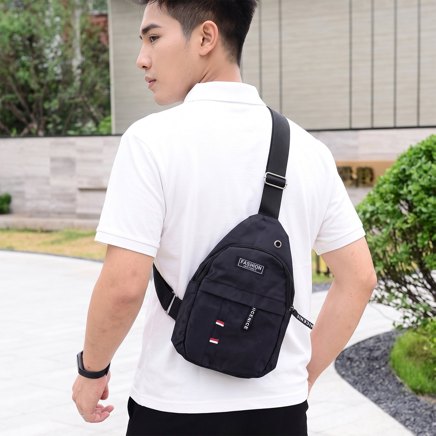 A man from behind wearing a black sling bag over a white polo shirt, looking over his shoulder.
