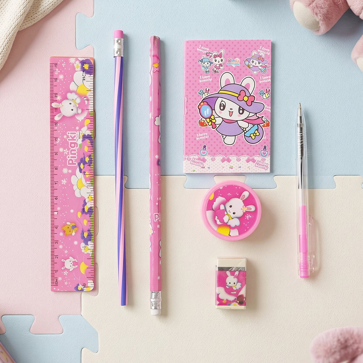 The pink 7-in-1 stationery set with bunny designs is arranged on a colorful blue and pink mat.