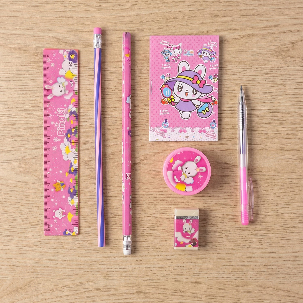The pink 7-in-1 stationery set with bunny designs, including a ruler, pencils, notebook, sharpener, and eraser on a wooden