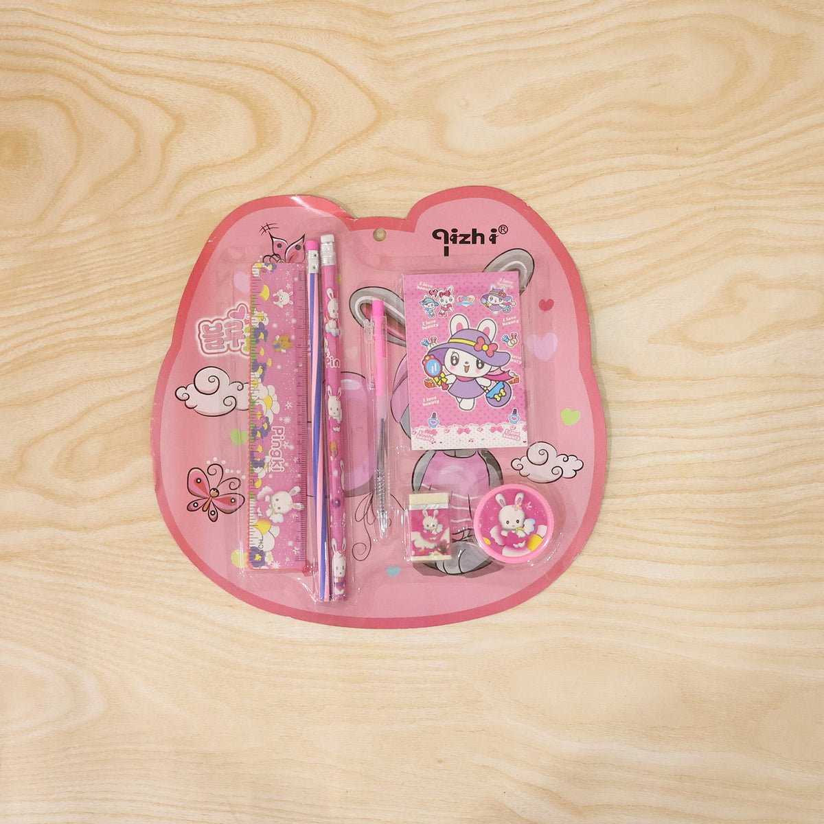 The pink 7-in-1 stationery set with bunny designs is sealed in clear plastic packaging on a wooden surface.