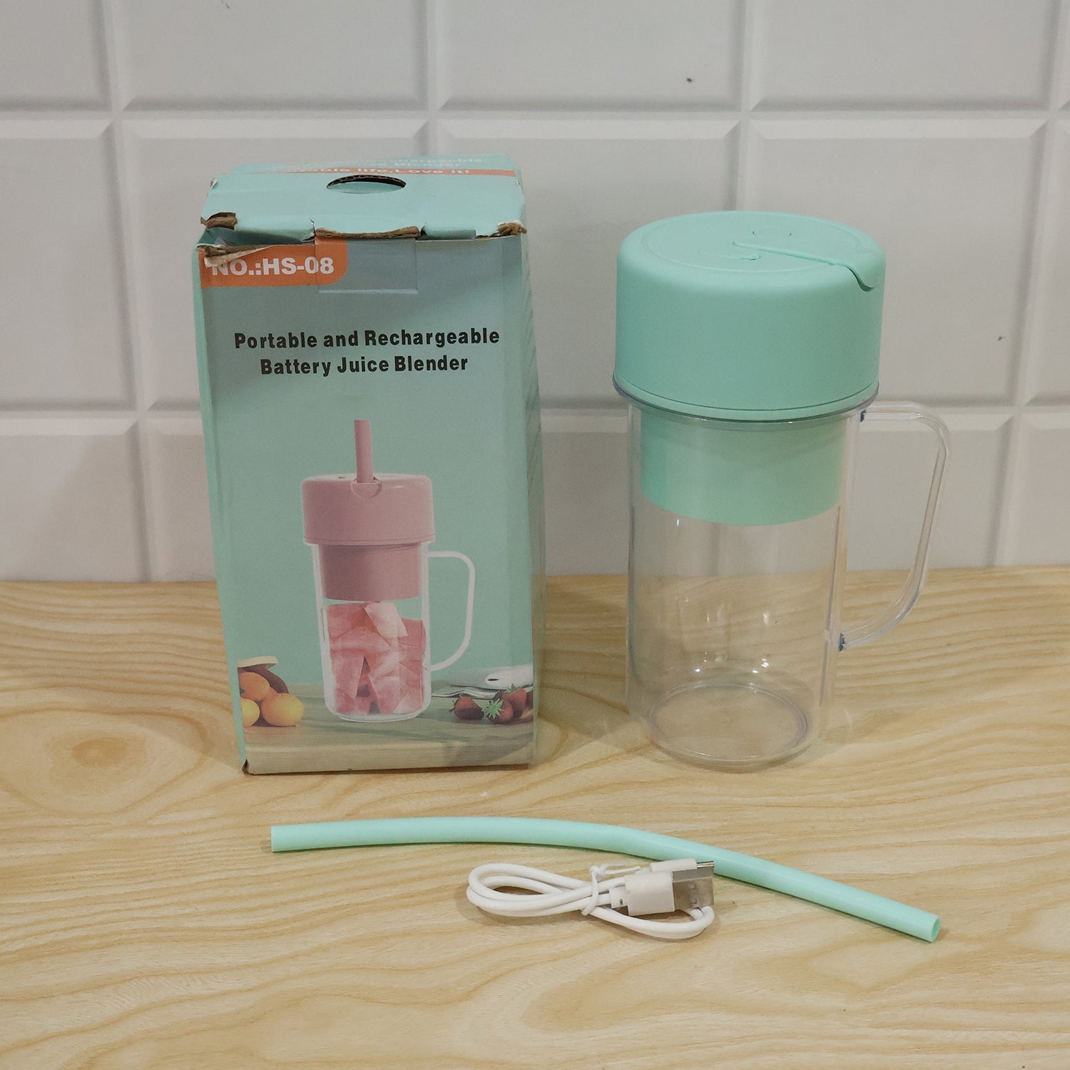 A mint green blender bottle, a matching straw, and a white USB cable are displayed next to its product box on a wooden