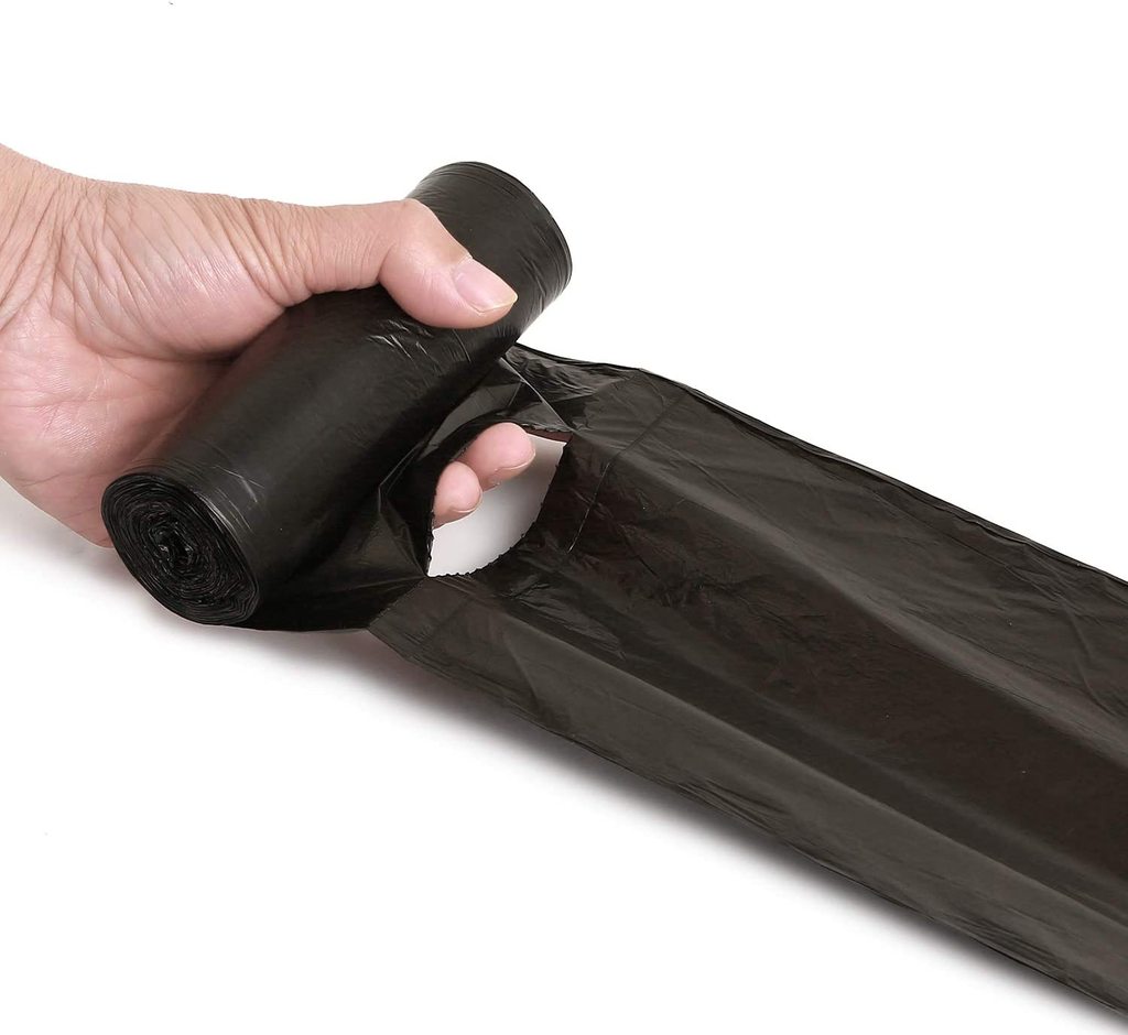 A hand unrolls a black garbage bag, pulling a single bag from the roll.