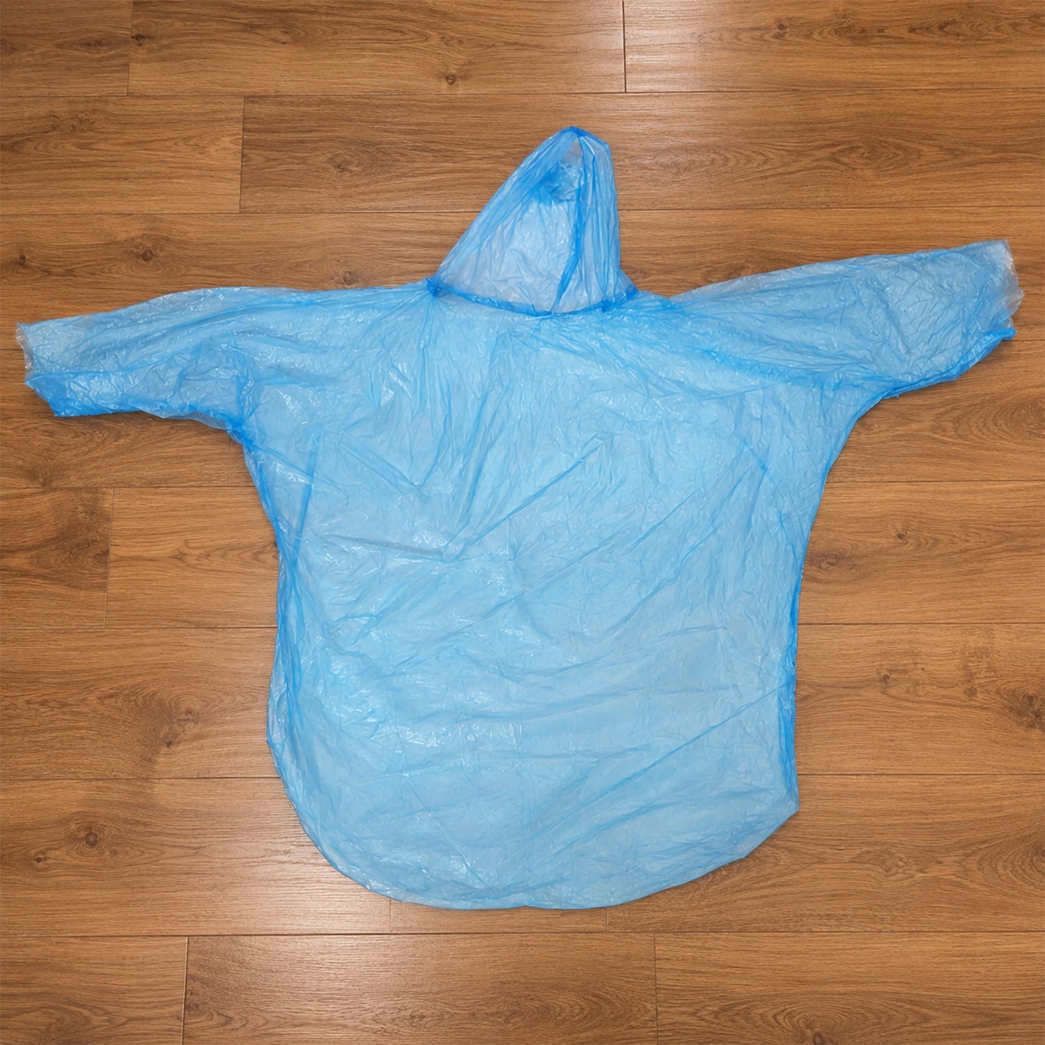 A translucent blue disposable rain poncho with a hood is spread out flat on a light brown wooden floor.