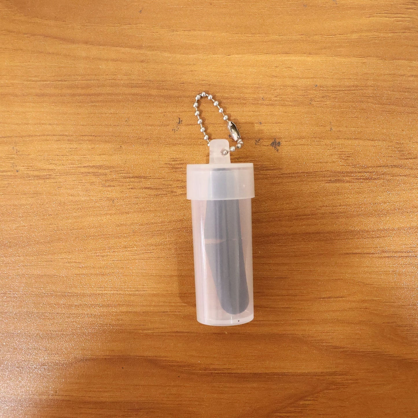 A clear plastic case with a silver keychain holds a pair of black earplugs, resting on a wooden surface.