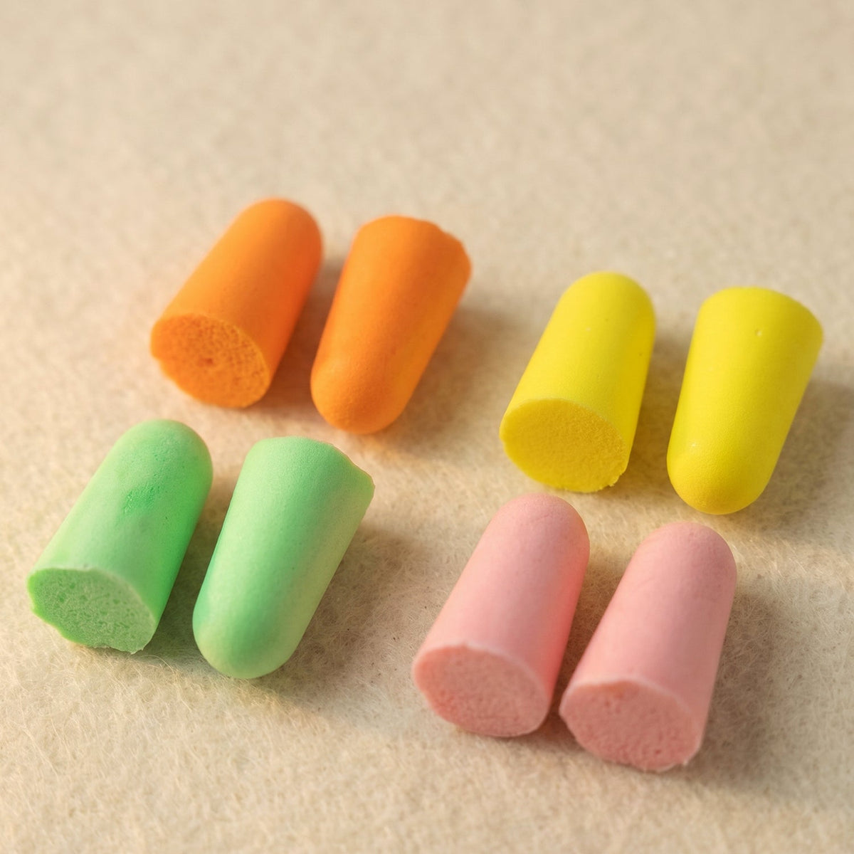 Eight foam earplugs in orange, yellow, green, and pink, with their cut ends visible, on a textured surface.