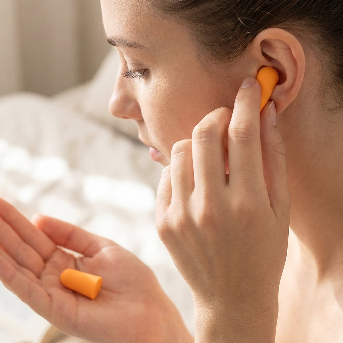 A woman inserting an orange earplug into her ear, holding another in her palm.