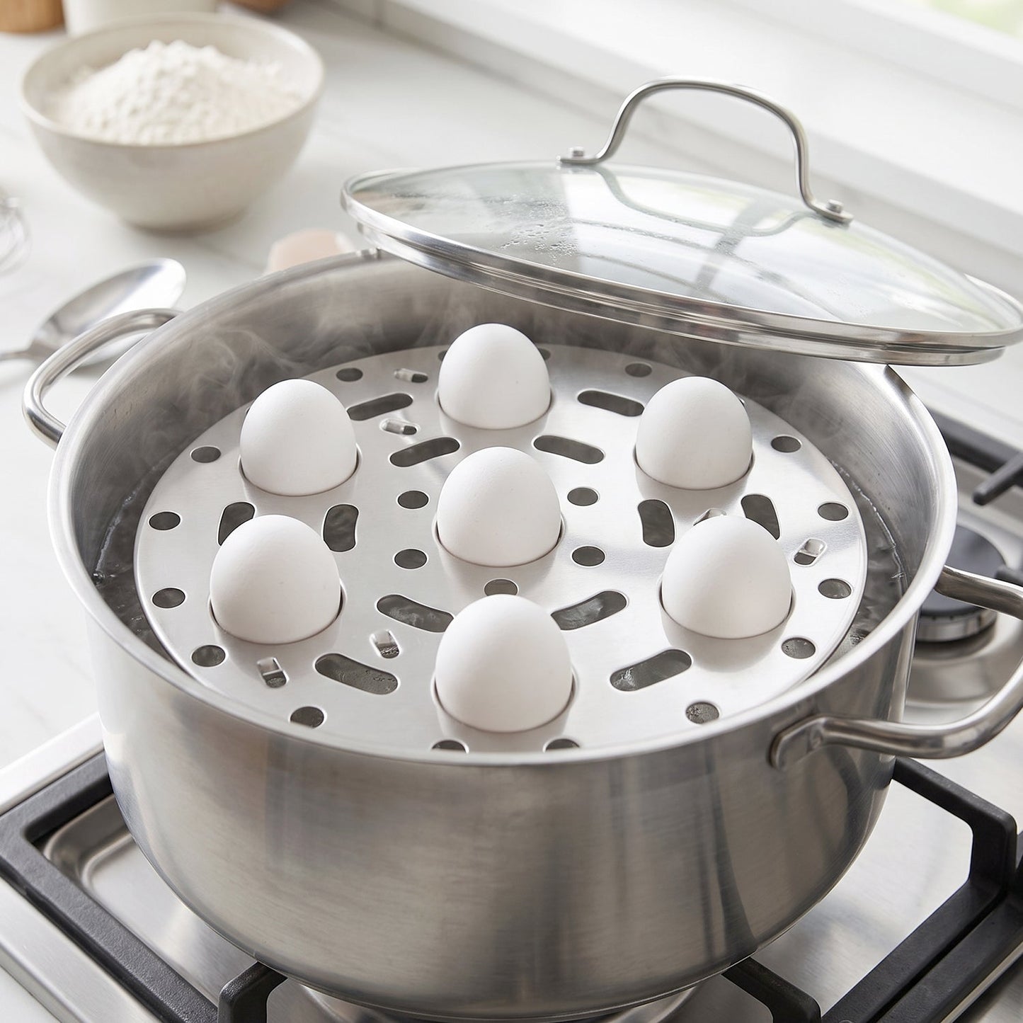 A stainless steel egg steamer rack with seven white eggs sits inside a steaming pot on a gas stove, with the pot lid propped