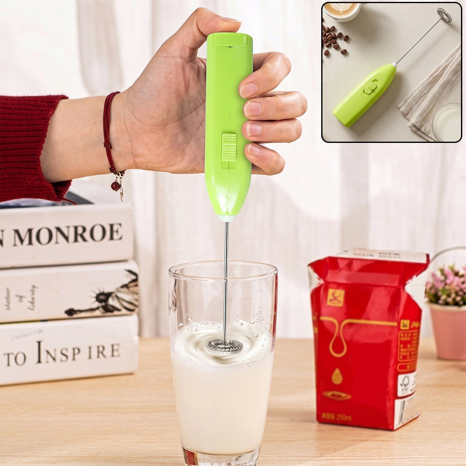 A hand holds a bright green electric frother, mixing milk in a clear glass, with books and a milk carton in the background