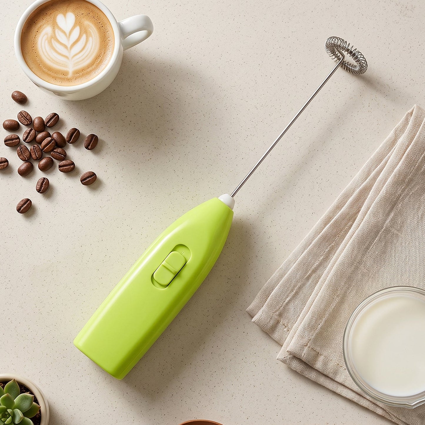 A bright green electric frother lies on a light surface next to coffee beans, a latte, a napkin, and a bowl of milk.