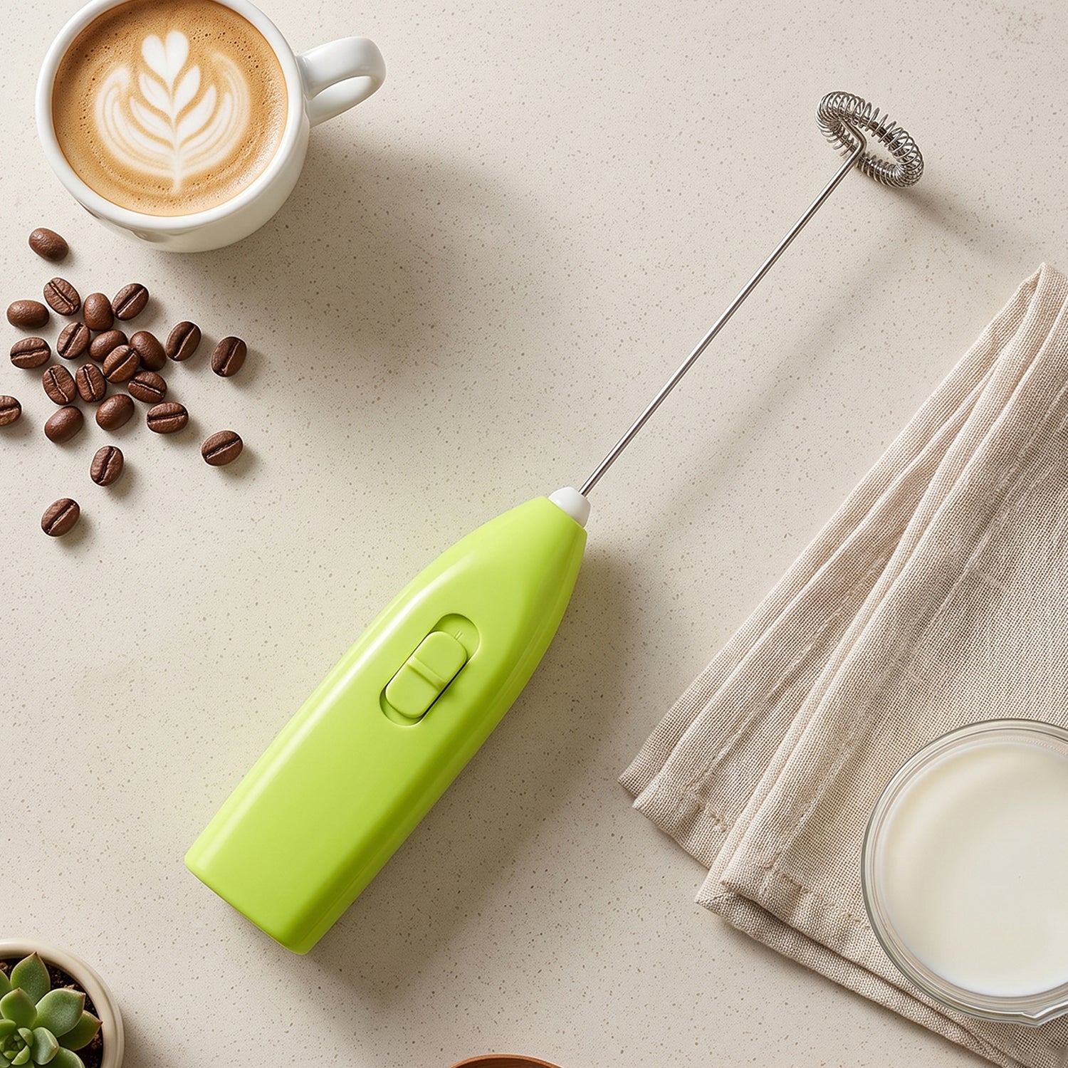 A bright green electric frother lies on a light surface next to coffee beans, a latte, a napkin, and a bowl of milk.