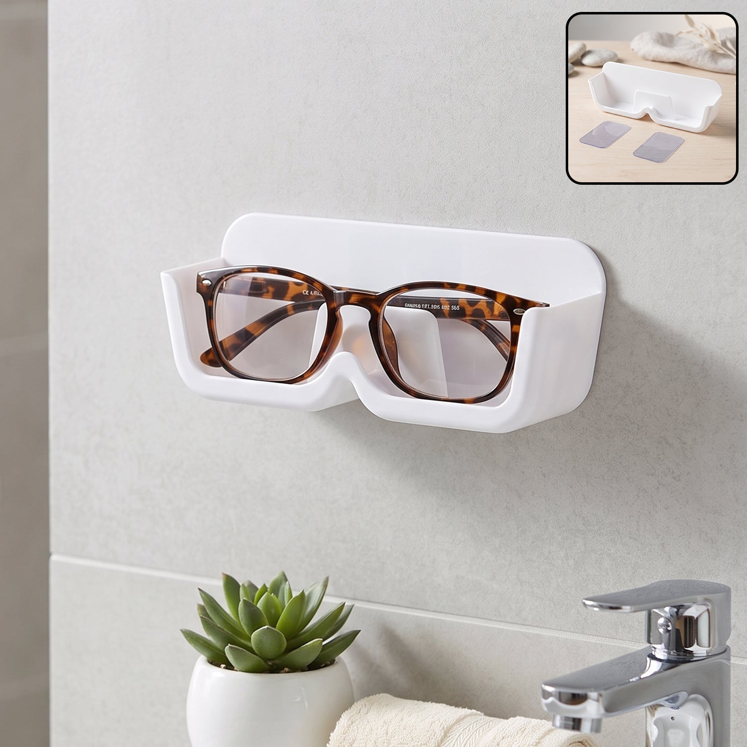 White plastic wall-mounted eyewear holder with tortoise-shell glasses, above a sink with a small green plant