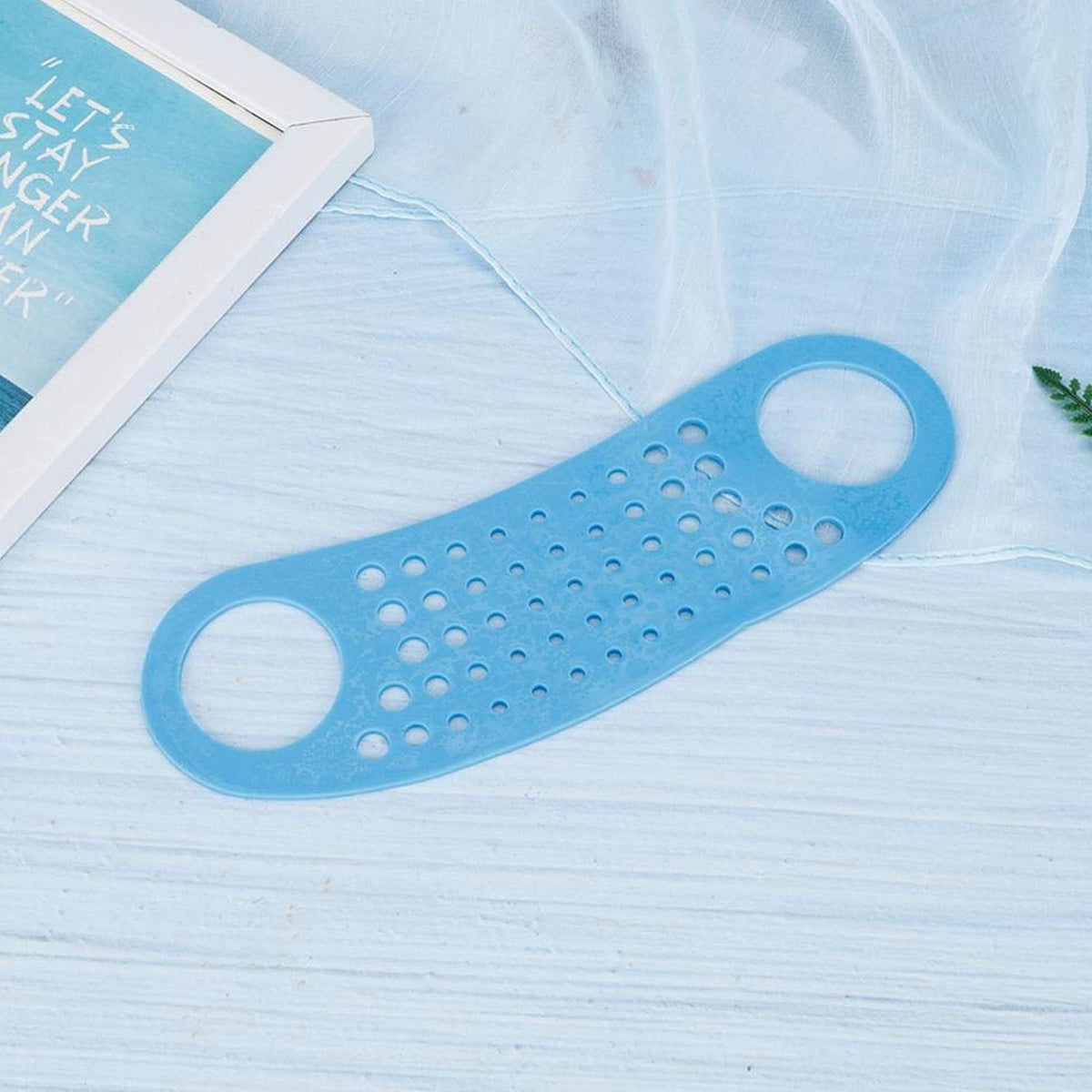 The blue silicone perforated strap lies on a light blue textured surface with a framed picture in the background.