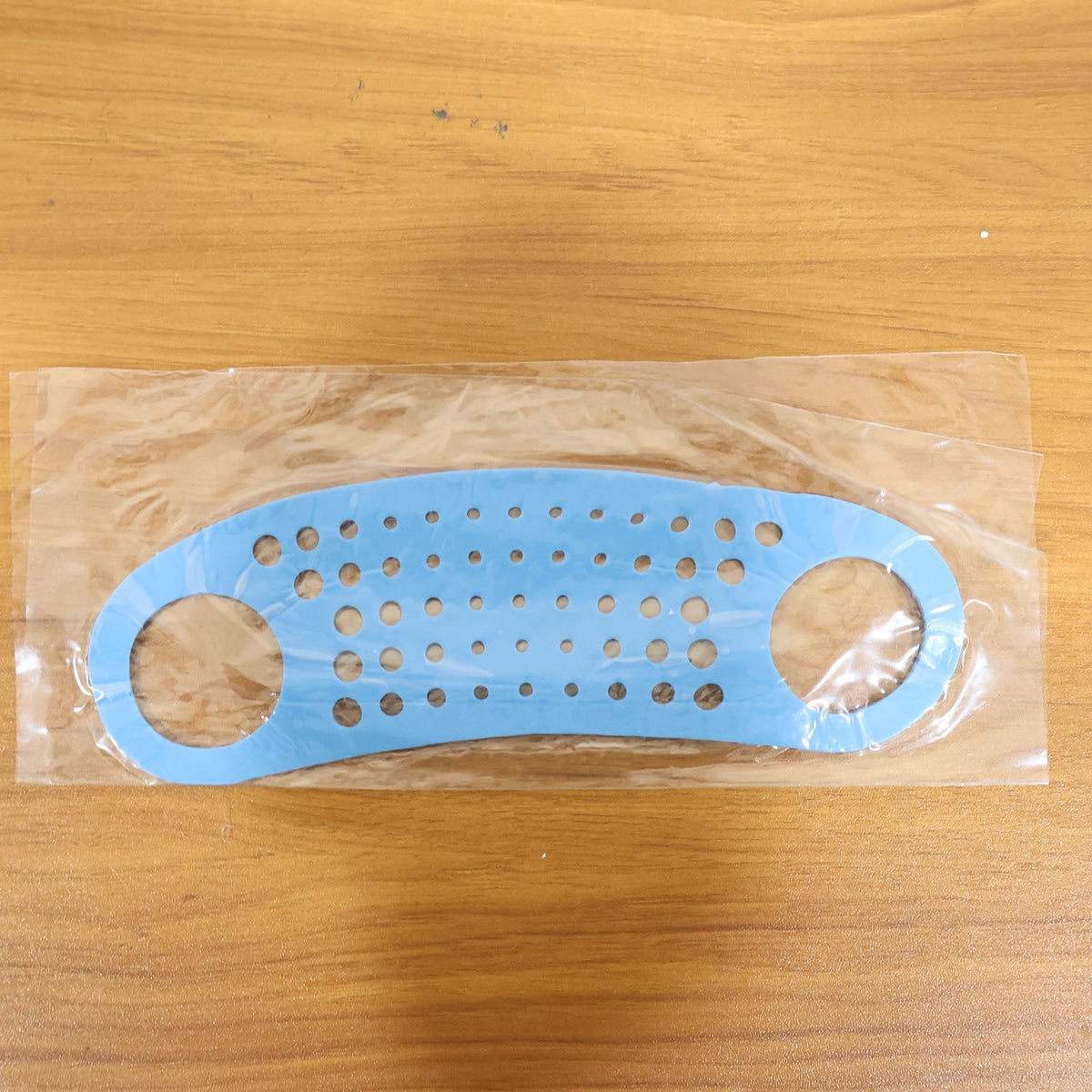The blue silicone perforated strap is sealed in clear plastic packaging on a wooden surface.
