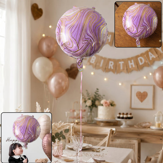 A purple and gold marble foil balloon floats above a decorated birthday party table with a cake and other balloons