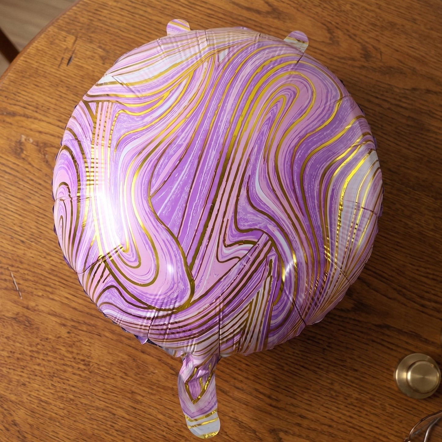 A close-up of a purple and gold marble foil balloon resting on a wooden table.
