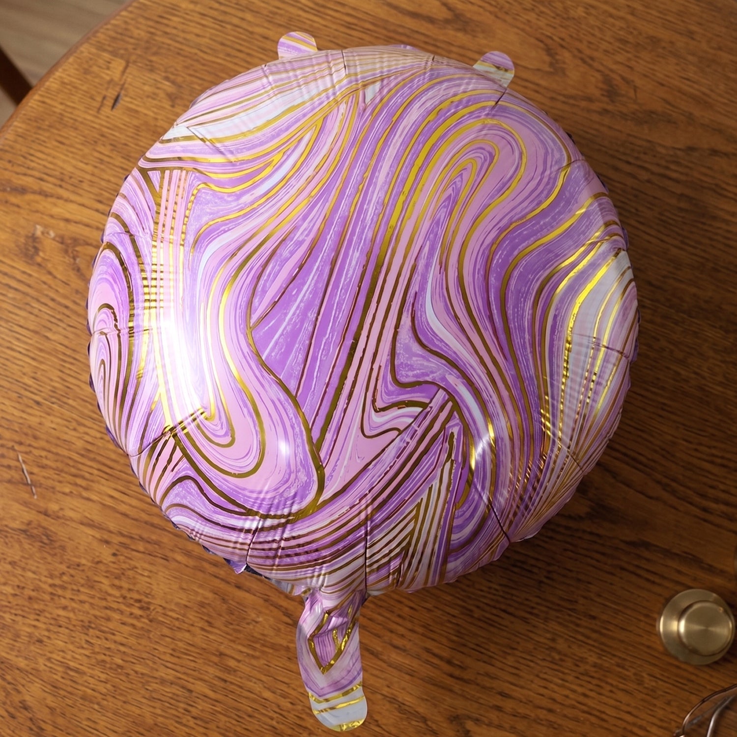 A close-up of a purple and gold marble foil balloon resting on a wooden table.