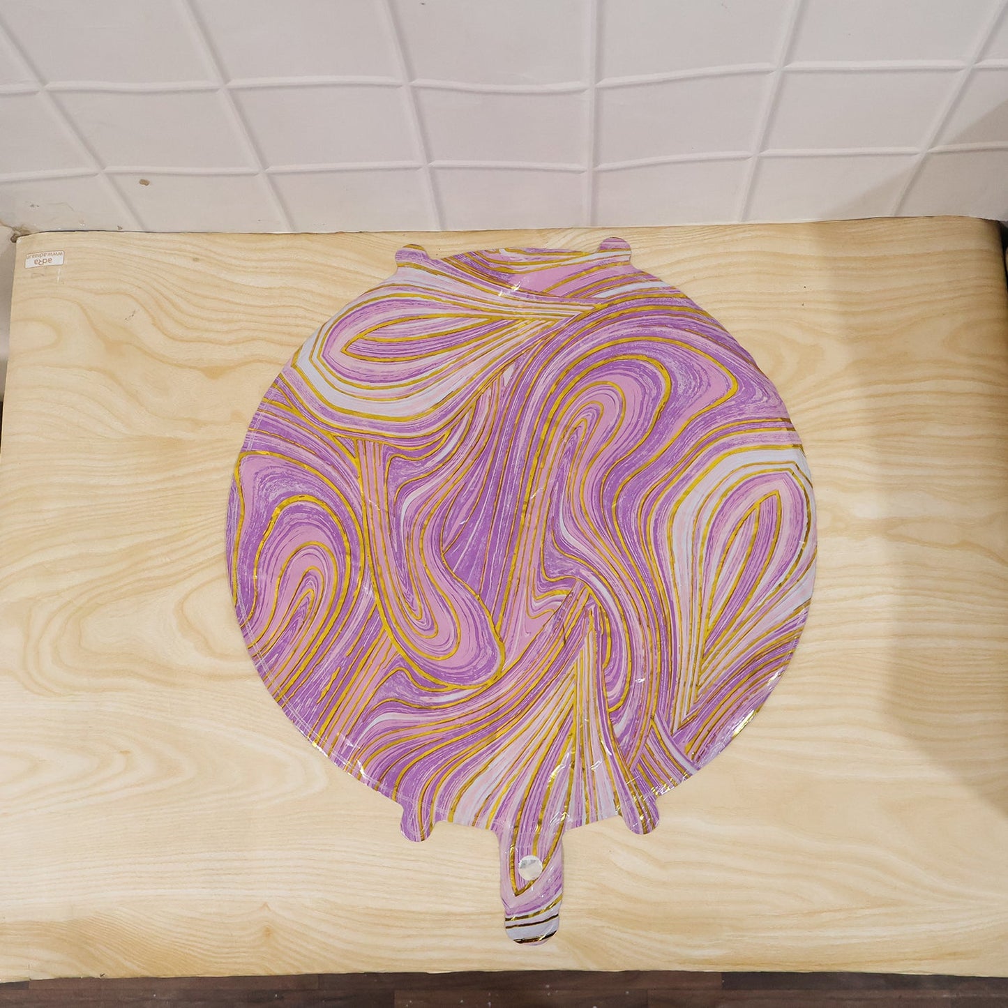 An uninflated purple and gold marble foil balloon lies flat on a light wooden surface.