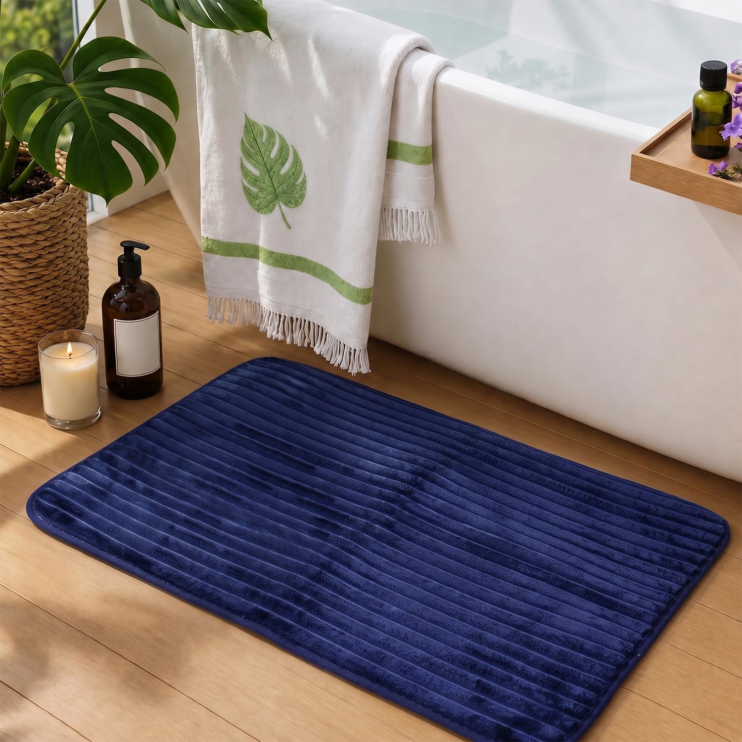 A navy blue ribbed memory foam bath mat is on a wooden floor in a bathroom with a white bathtub and plants.
