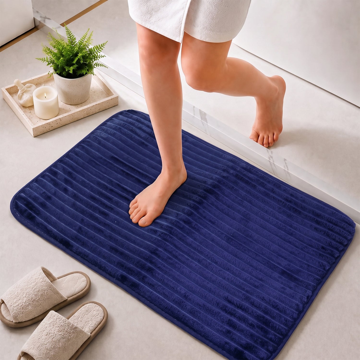A person's bare feet are shown stepping onto a navy blue ribbed memory foam bath mat next to a shower.