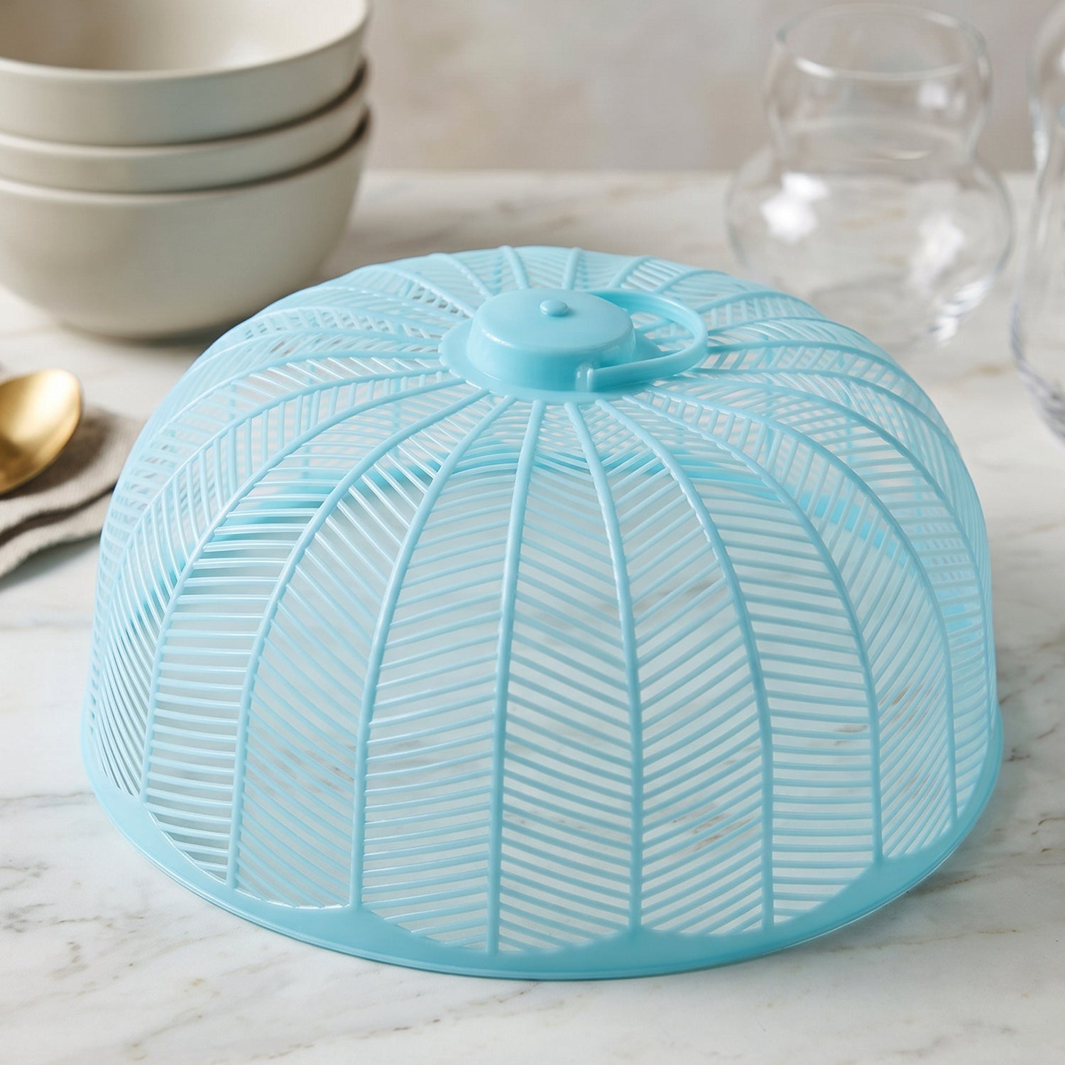 Light blue plastic mesh food cover dome on a marble countertop with blurred kitchenware in the background.