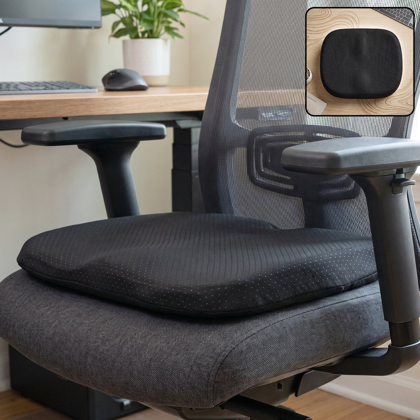 Black ergonomic memory foam seat cushion on a grey office chair with a small inset of the cushion on a wooden desk.