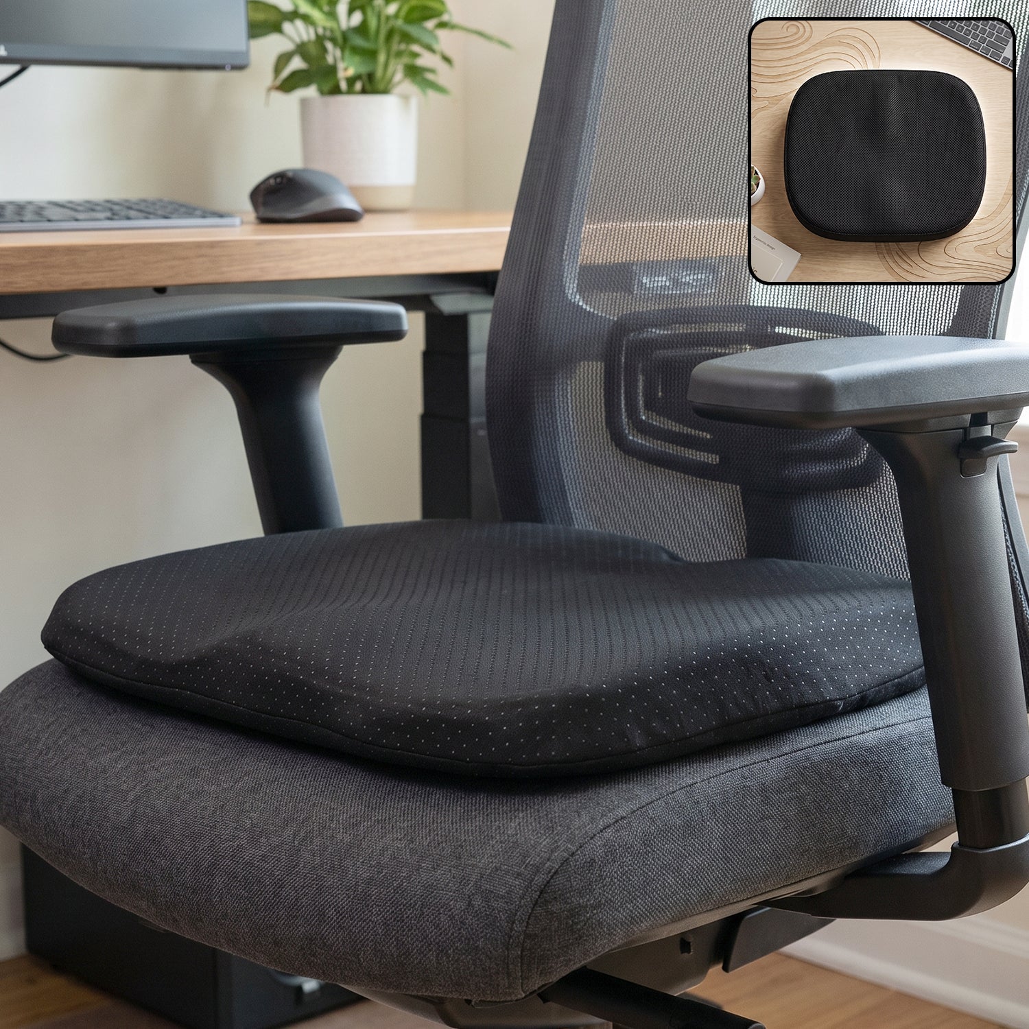 Black ergonomic memory foam seat cushion on a grey office chair with a small inset of the cushion on a wooden desk.