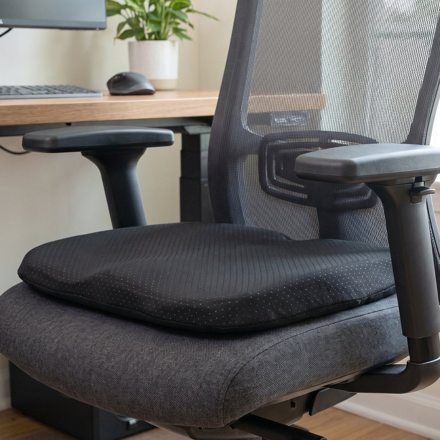 Black ergonomic memory foam seat cushion on a grey office chair in an office setting.