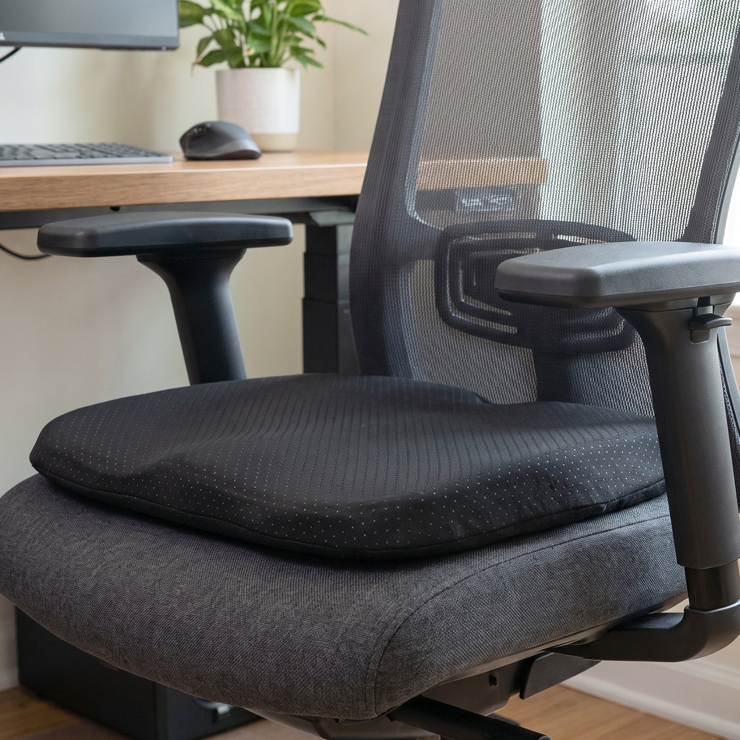 Black ergonomic memory foam seat cushion on a grey office chair in an office setting.