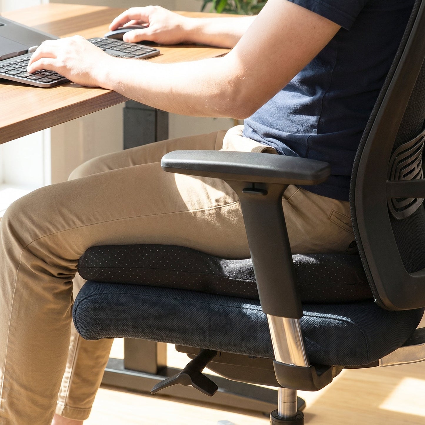 A person sitting on a black ergonomic seat cushion in an office chair, working at a desk.