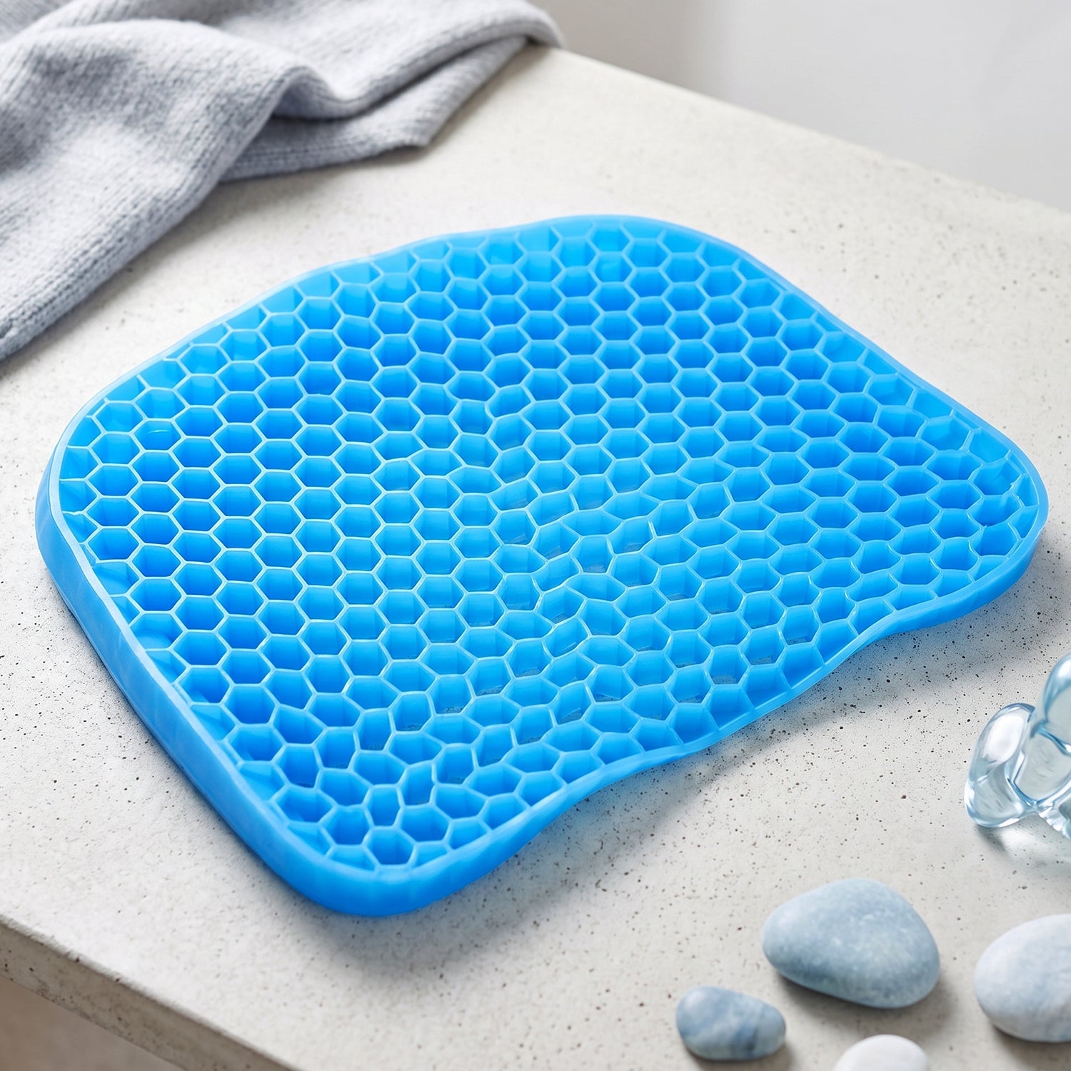 A bright blue honeycomb gel seat cushion resting on a light grey surface with decorative stones.