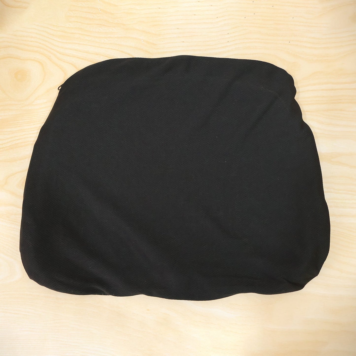 A black fabric cover for a seat cushion, laid flat on a light wooden surface.